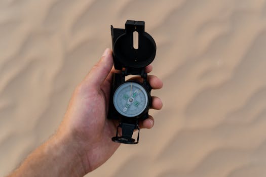 Hand holding a compass over sandy desert terrain, symbolizing navigation and adventure.