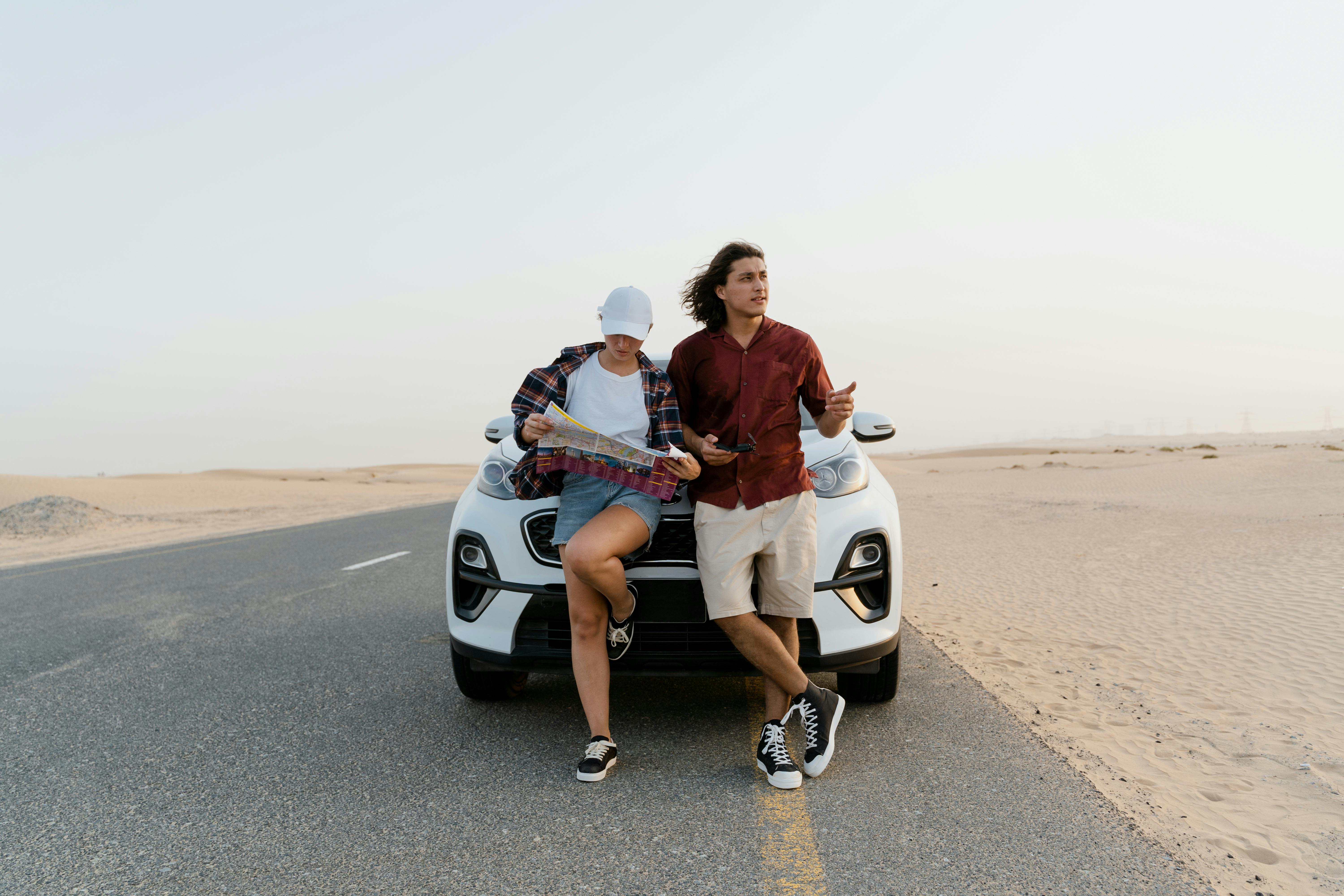 man and woman holding a map while standing in front of the white car