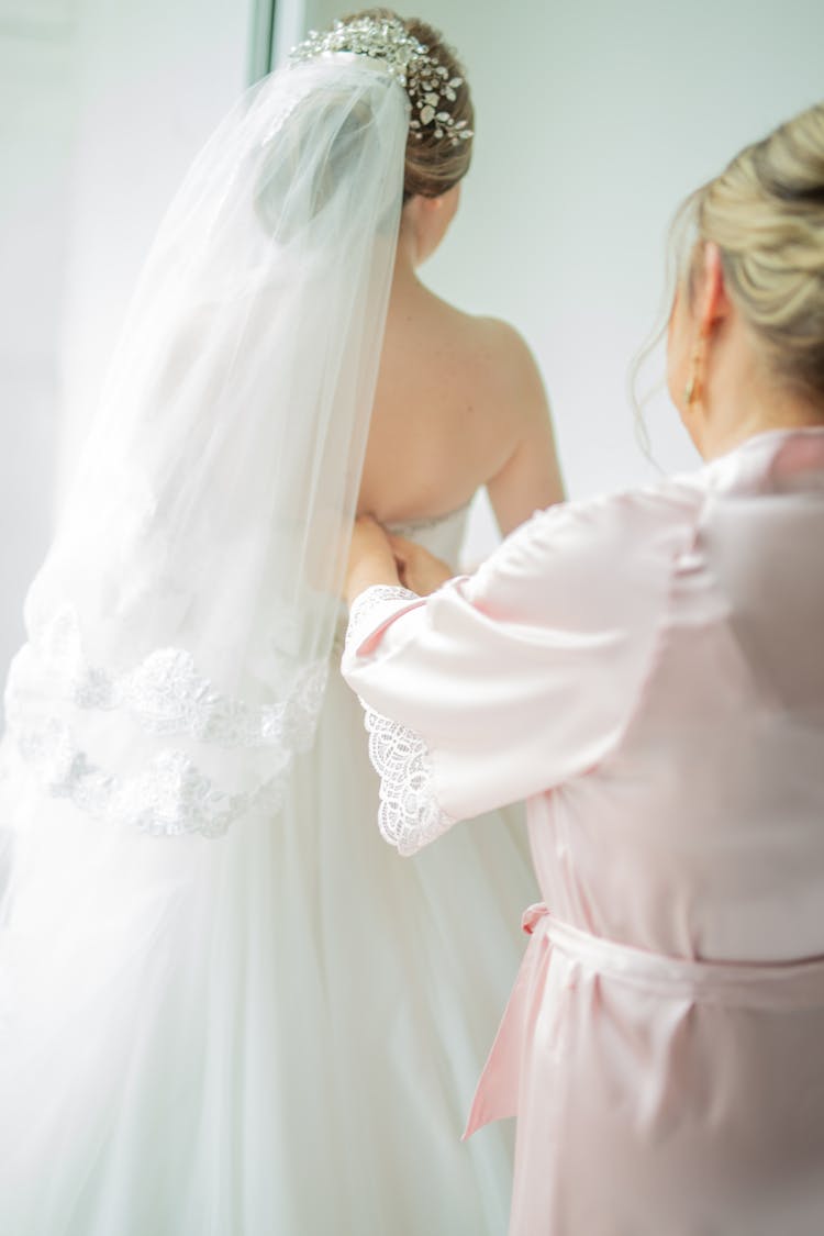 Woman Zipping The Gown Of A Bride