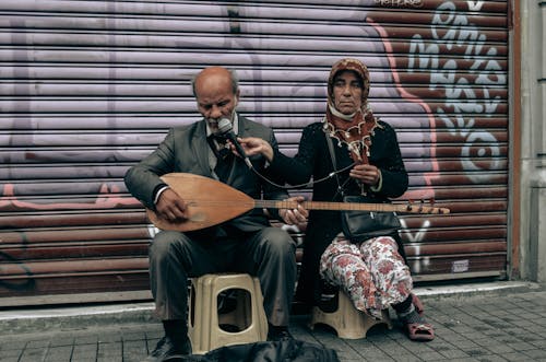 Man Playing a Saz and Woman Holding a Microphone on a Sidewalk in City 