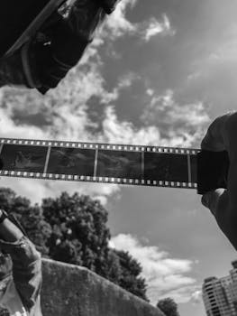 Artistic shot of a film strip held against a bright sky, showcasing a vintage photography theme.