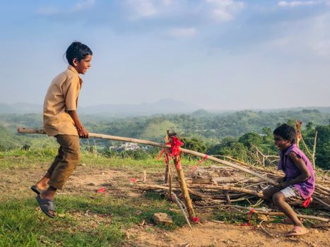 Two children enjoy a day outdoors playing on a seesaw with scenic views.