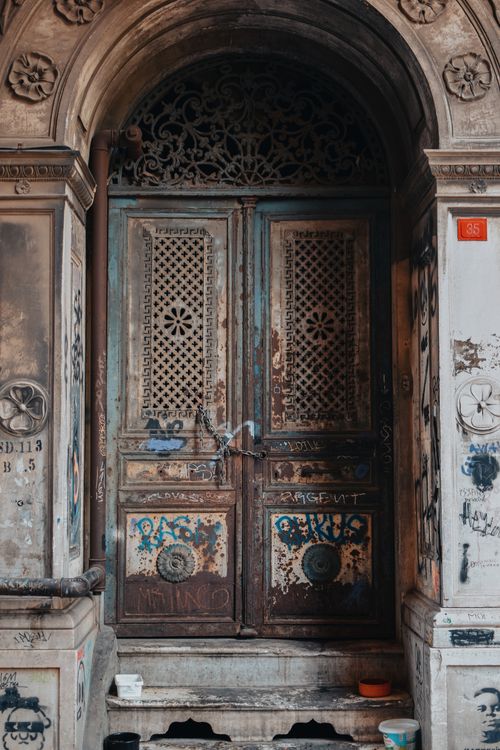 Free Detailed view of an ornate, weathered wooden door surrounded by graffiti, showcasing urban decay. Stock Photo
