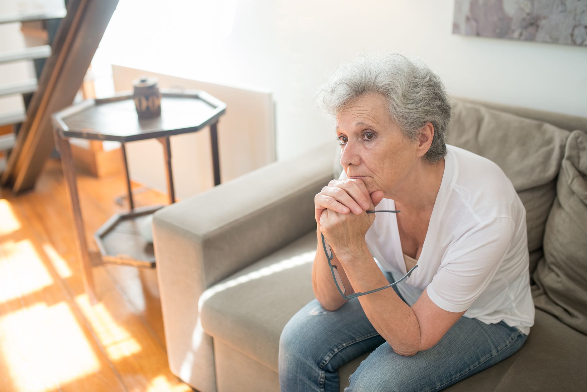 methylene blue brain health long covid older adults — Elderly woman sitting pensively on a couch indoors, embodying thoughtful reflection.
