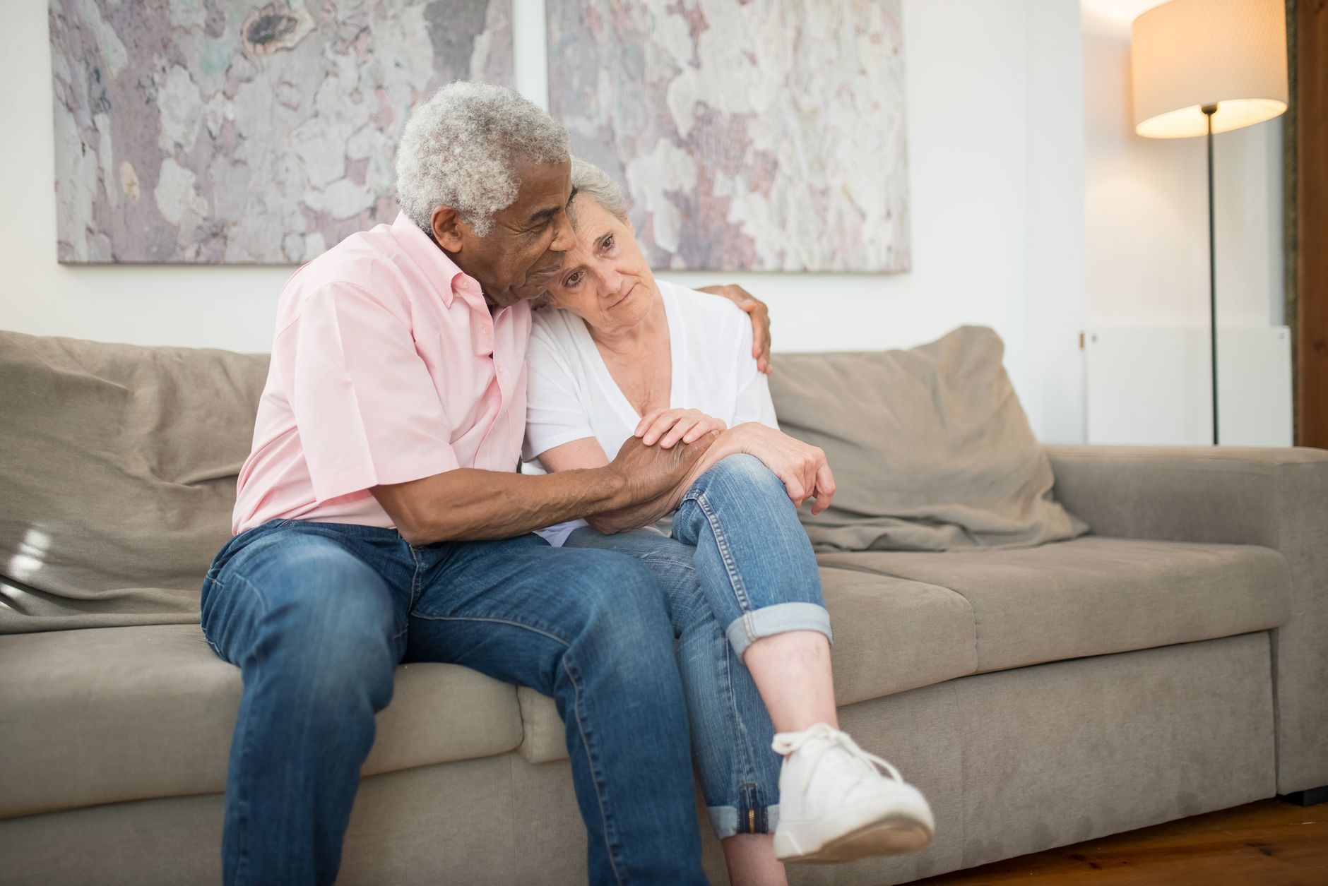 Worried adult daughter sitting beside elderly father lying in bed at home