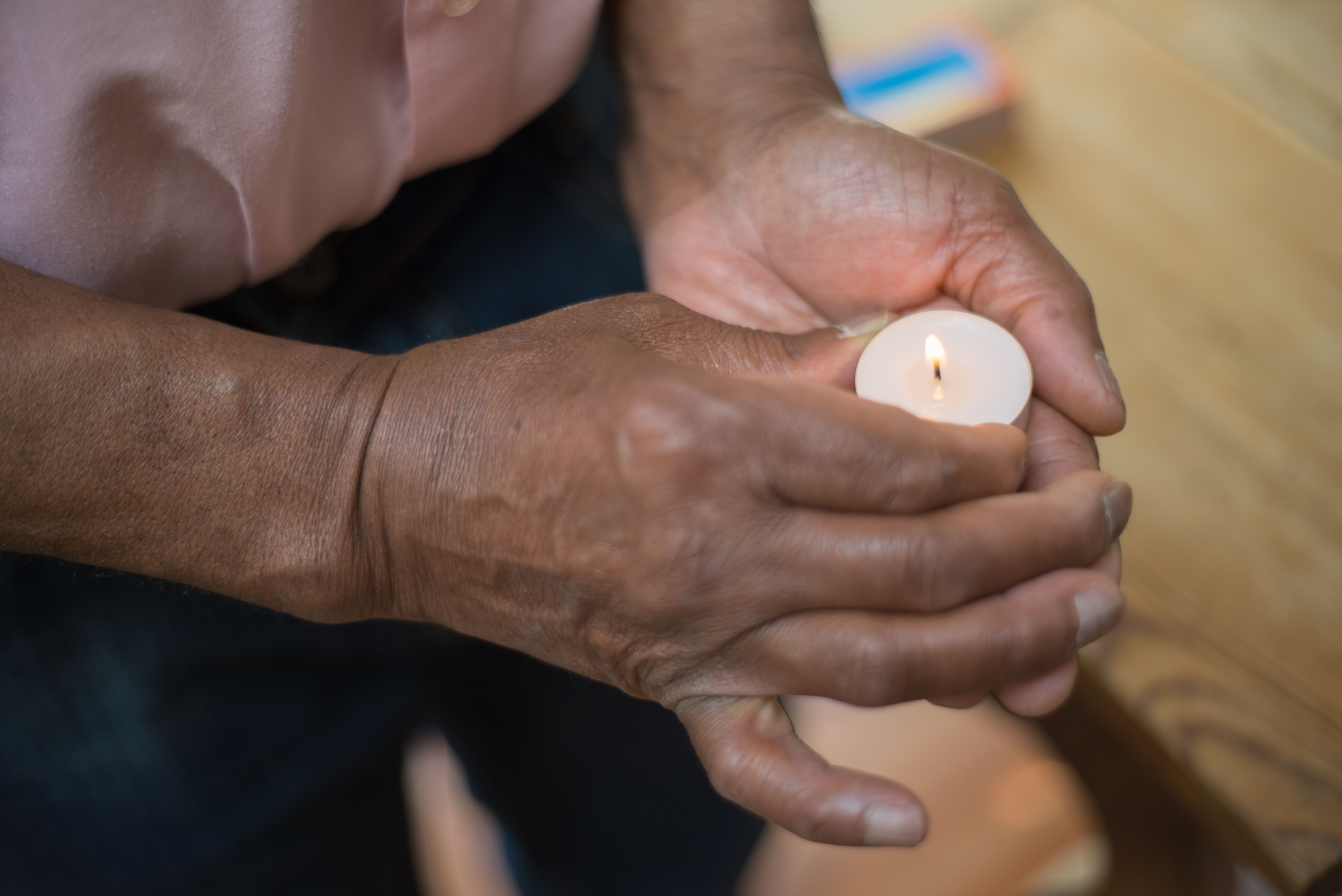 Detailed image of hands holding a glowing tealight candle indoors.