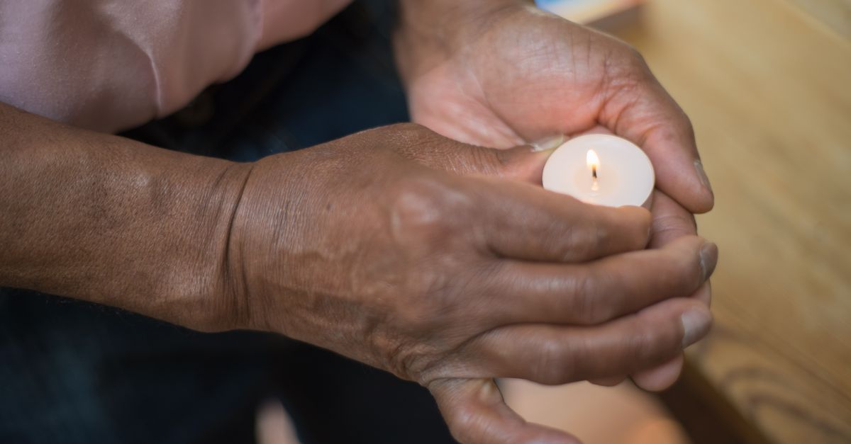Detailed image of hands holding a glowing tealight candle indoors.