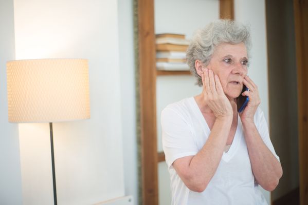 Elderly woman with white hair talking on phone, appearing concerned, indoors