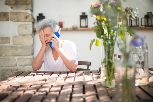 Free A distressed senior woman sitting outdoors, holding a cellphone, and showing emotion. Stock Photo