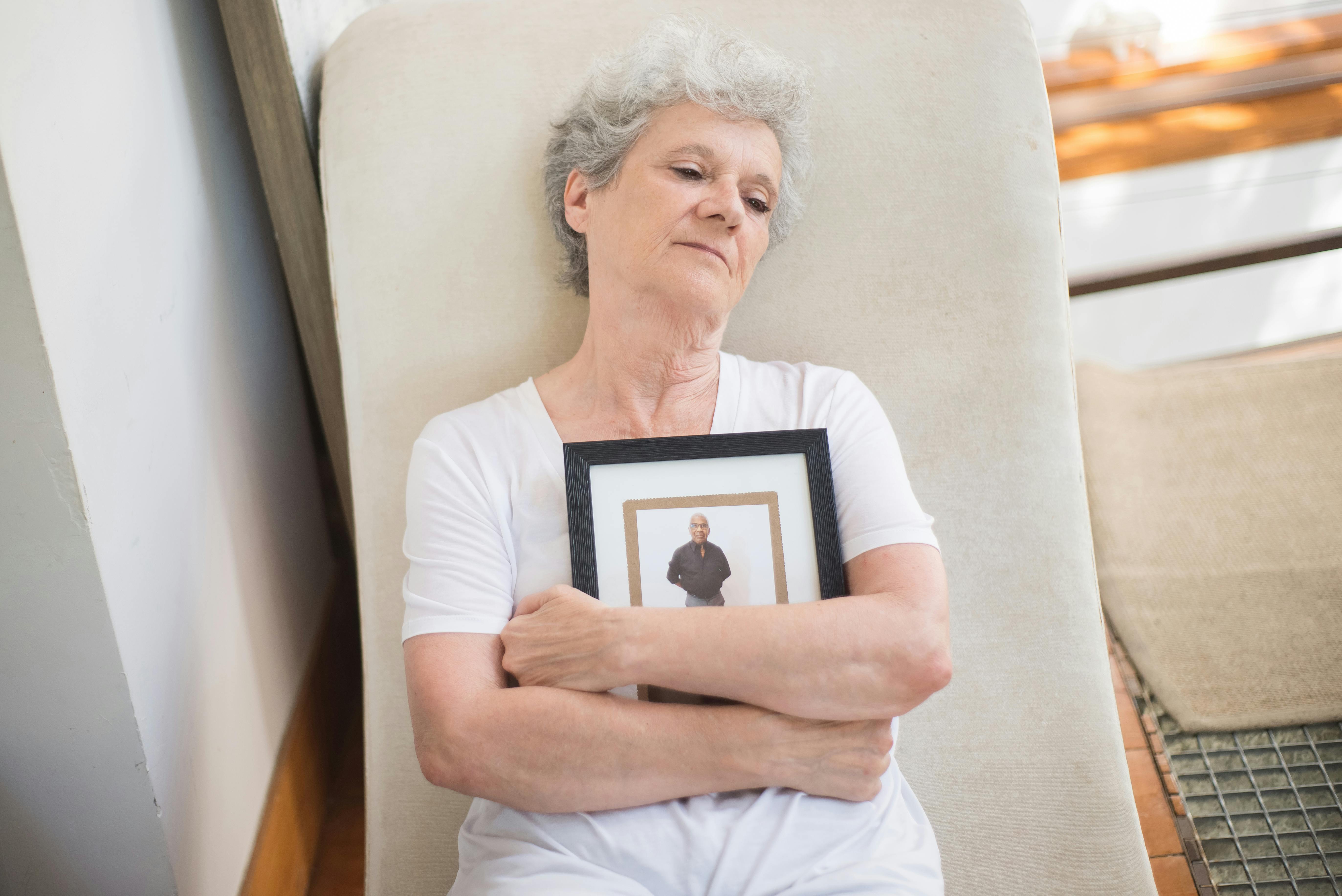 Elderly woman holding a photo frame, expressing emotion in a peaceful setting.