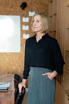 Mature businesswoman stands confidently in a modern office, ready for a meeting.