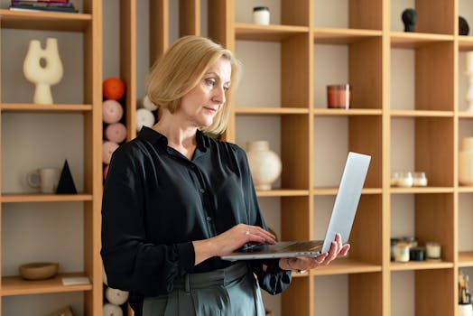 Elderly woman working on a laptop in a stylish indoor setting with wooden shelves.