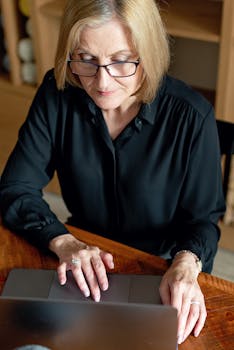 Senior businesswoman with glasses working intently on a laptop indoors.