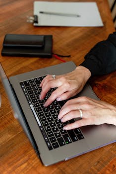 A close-up shot of a woman typing on a laptop at a wooden desk, capturing focus and productivity.