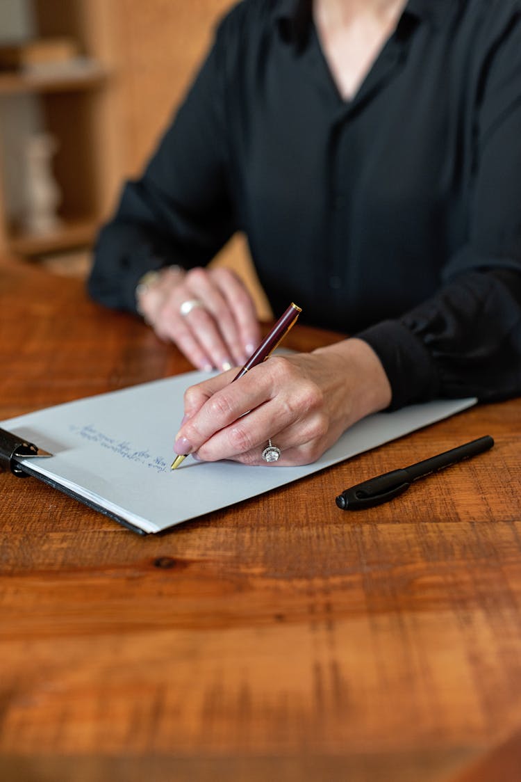 A Person Writing On A Piece Of Paper On A Clipboard