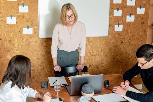Three colleagues engaged in a collaborative meeting, surrounded by notepads and a laptop in a modern office.