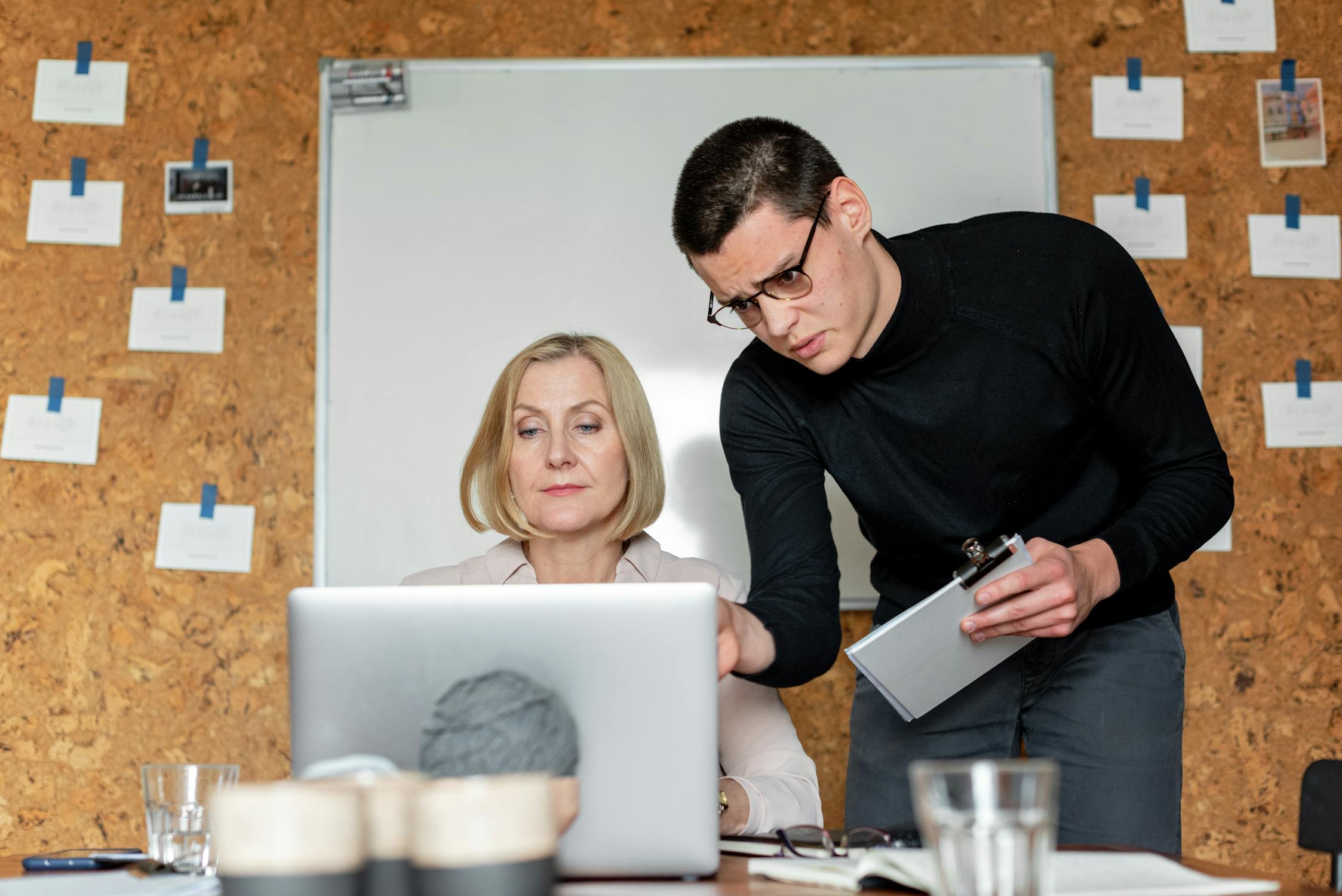 man in black sweater holding white notebook beside woman sitting at the table