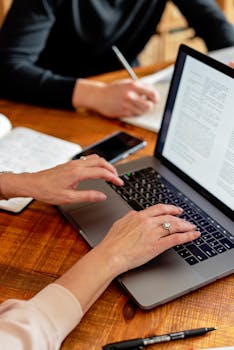 Two people working on business documents and a laptop at a wooden desk.