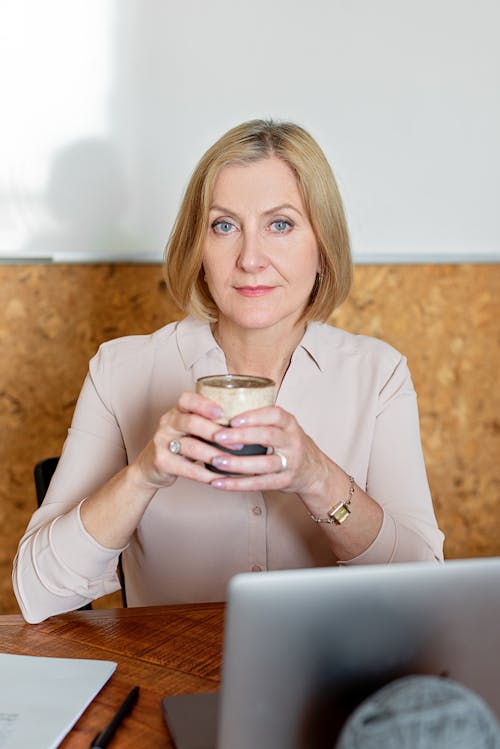 Free A Woman Holding a Cup of Tea While Sitting at Her Work Desk Stock Photo