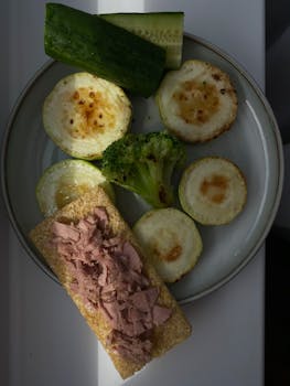 A nutritious dish featuring roasted zucchini, cucumber, broccoli, and tuna on a plate.