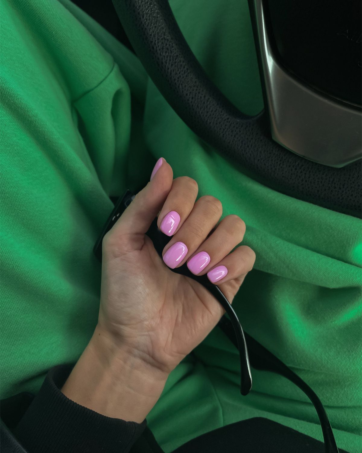 A stylish close-up shot of a hand with pink nail polish, set against a vibrant green background in a car interior.