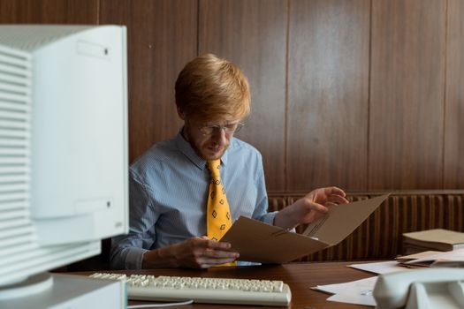 Vintage office scene with a man reviewing documents on an old computer desk.