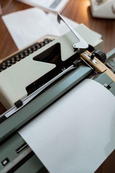 Close-up of a classic vintage typewriter with a blank sheet of paper on a wooden desk.