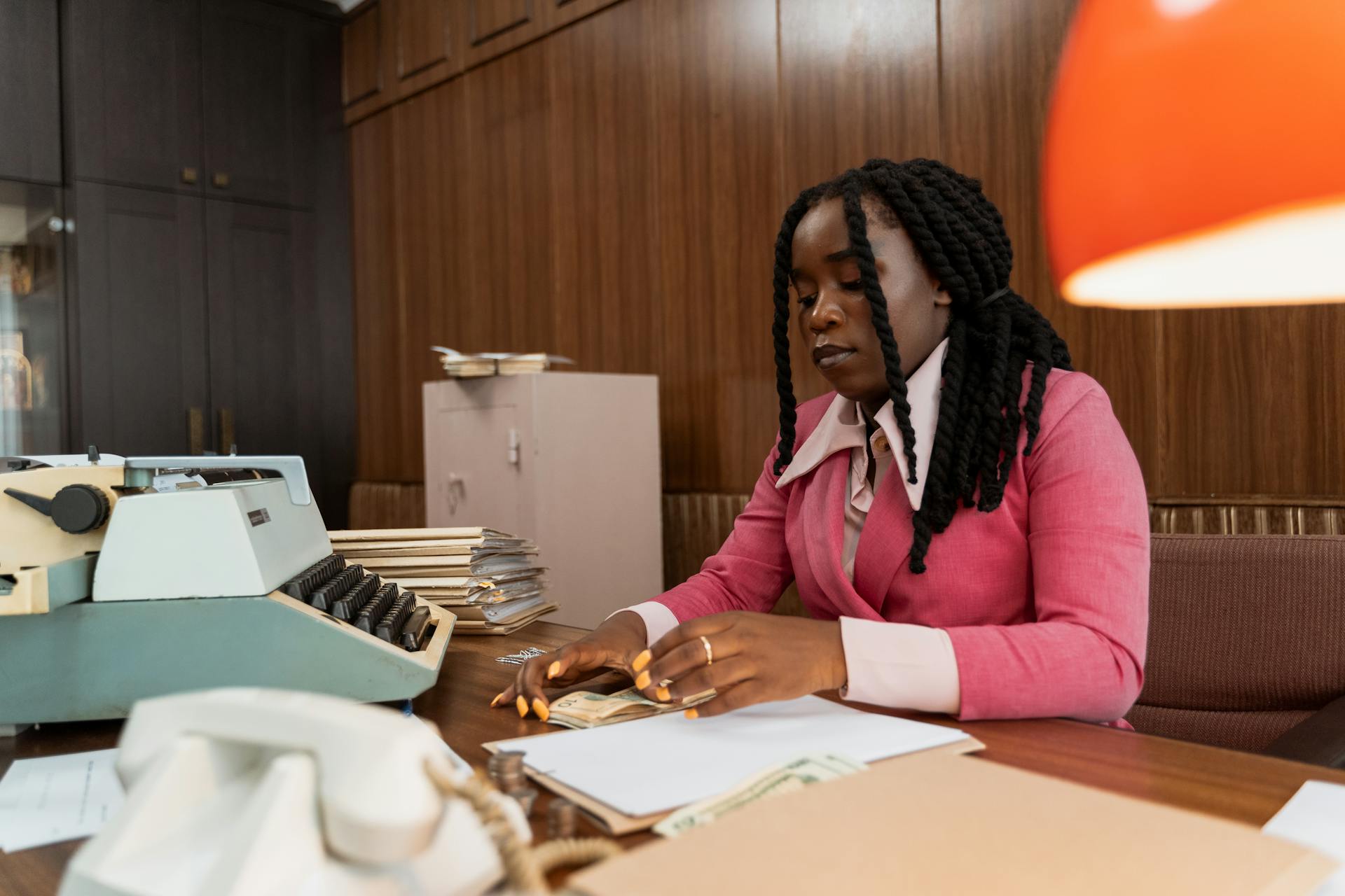 African American woman in business attire counting money at a vintage office desk.