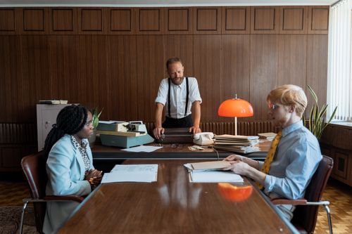 Free Three colleagues having a discussion in a vintage-style office with a typewriter and wooden paneling. Stock Photo