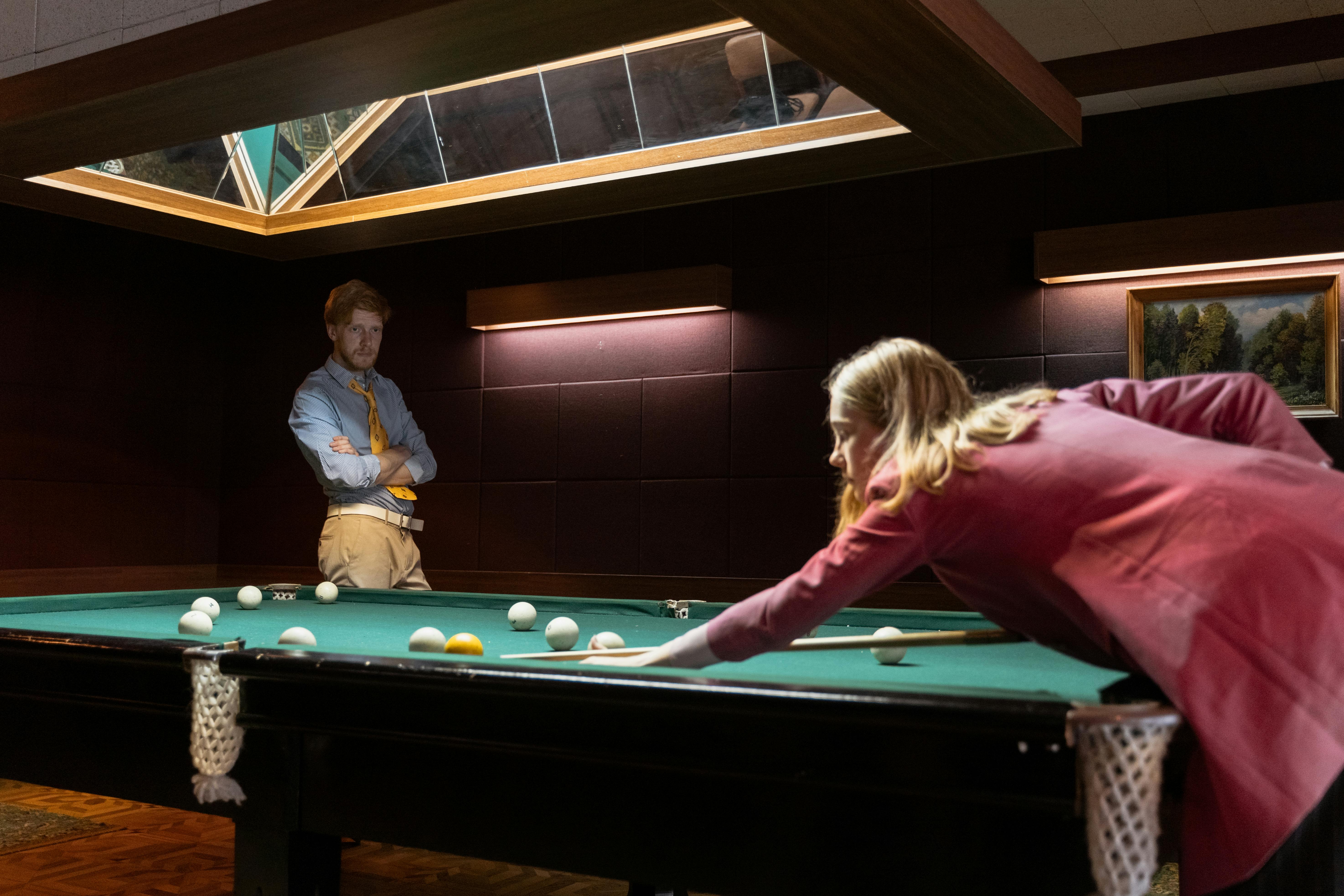 a man looking at a woman playing billiard