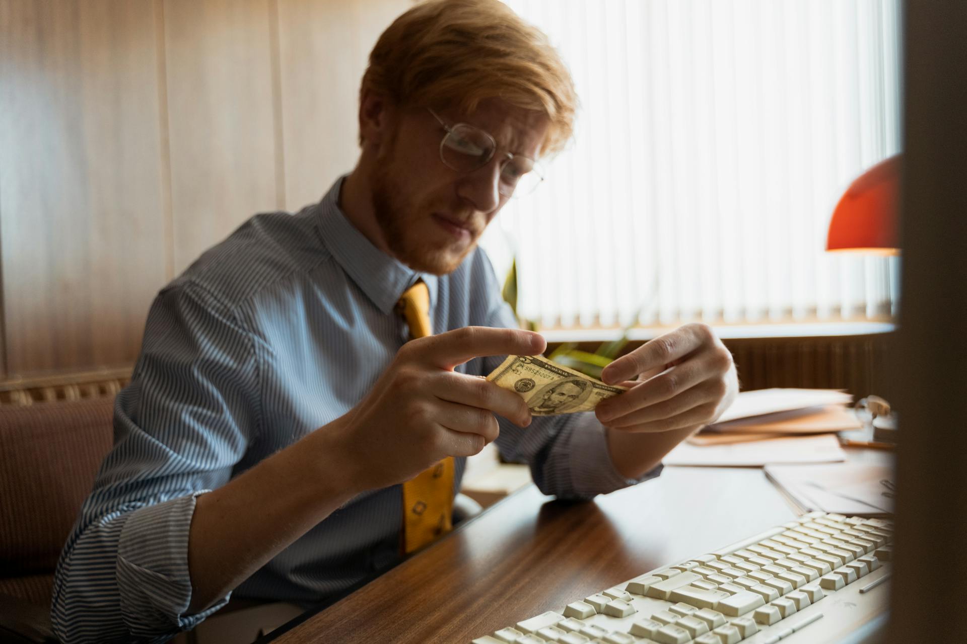 Male entrepreneur intensely examines money at his office desk, representing finance.