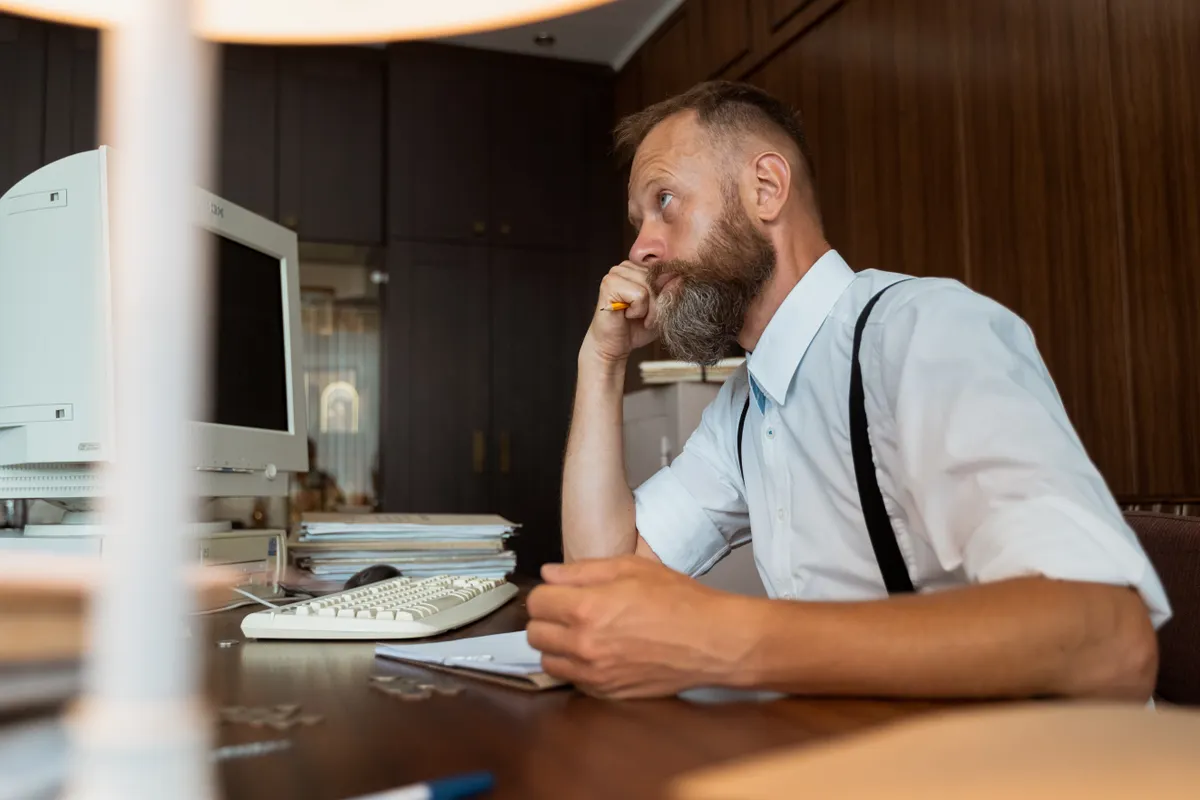 A man sitting in an office, thinking, with his hand near his chin