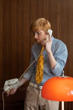 Caucasian man with red hair using a vintage telephone indoors, showcasing a classic professional setting.