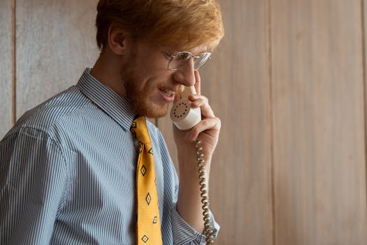 A businessman with glasses making a phone call in a retro office setting.