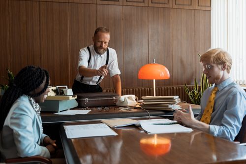 Free A vintage office meeting with three adults discussing documents around a table. Stock Photo