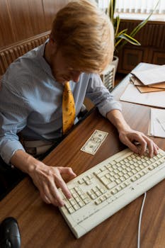 Retro style businessman typing on keyboard with dollar bill on desk.