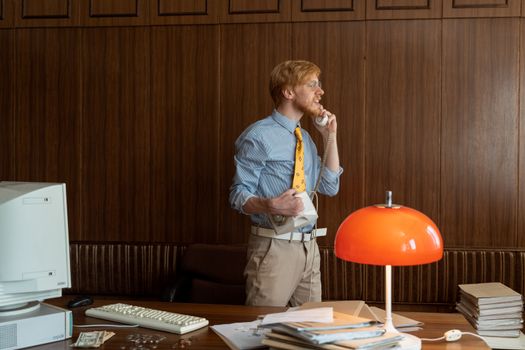 A man in retro attire talking on a corded phone in a vintage office setting.