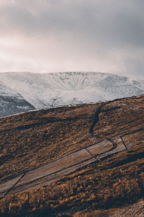 Free A scenic view of snowy mountains and a winding path through an autumn hillside, capturing nature's contrast. Stock Photo