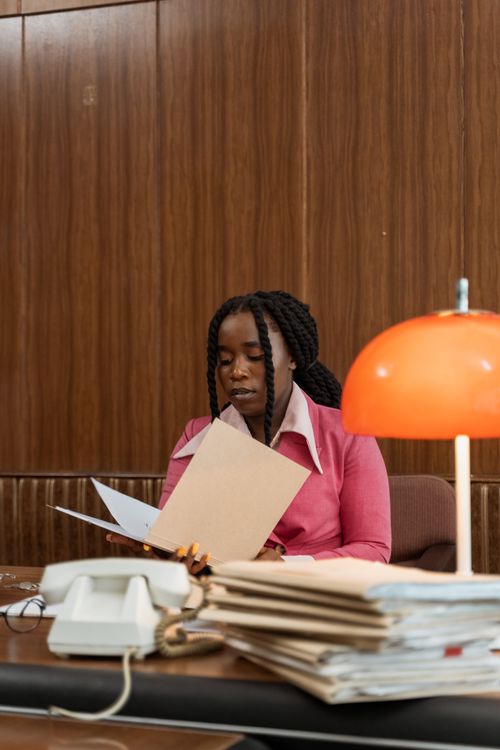 Free Businesswoman in a retro office holding documents at a desk with a lamp. Stock Photo