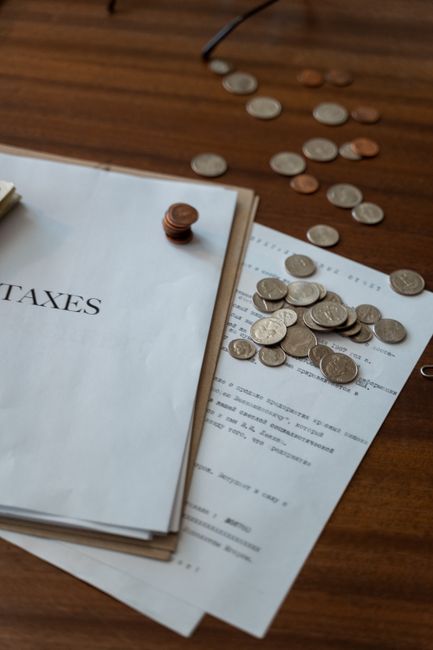 Photo by MART PRODUCTION Close-up of tax documents and scattered coins on a wooden desk, representing finance and taxation.