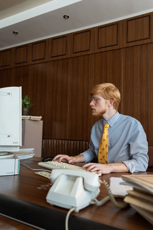 A Man Looking at His Computer Monitor while Typing on the Keyboard