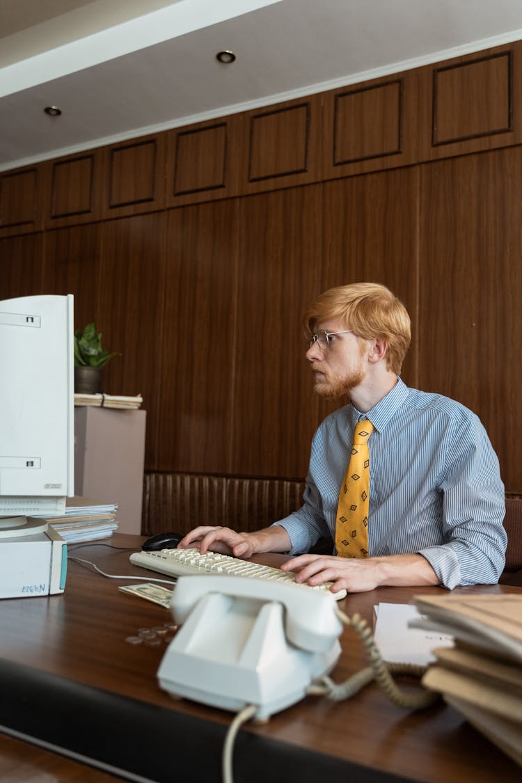 A Man Looking At His Computer Monitor While Typing On The Keyboard