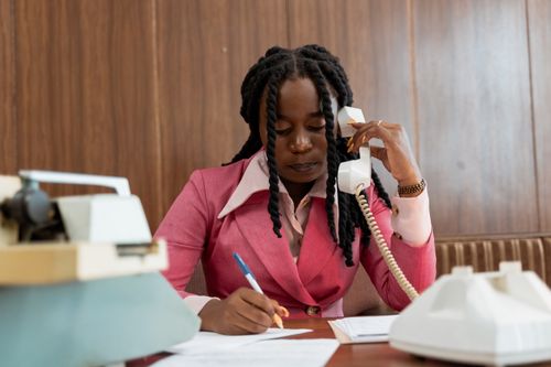 Free Professional woman in 80s style business attire making notes during a phone call. Stock Photo