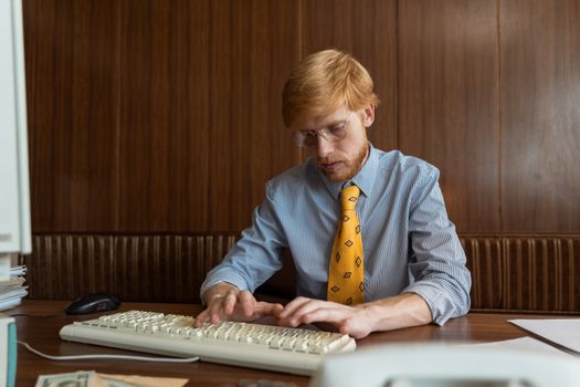A concentrated man working at his desk, typing on a vintage keyboard with a computer mouse nearby.