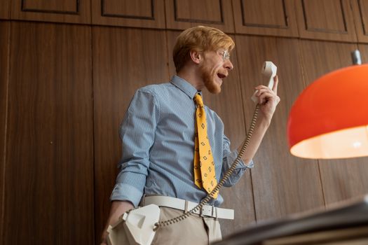 Smiling man with a vintage phone indoors, expressing emotions.