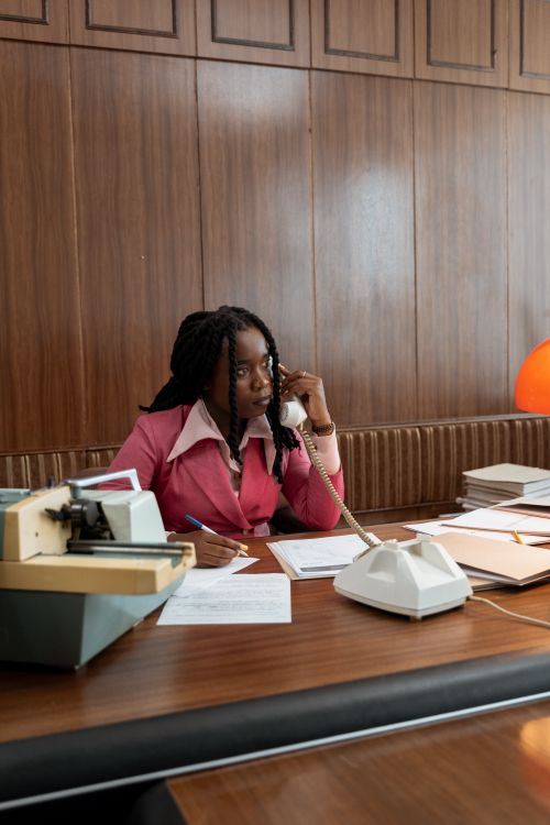 Free African American woman working at a retro office desk with a vintage telephone and typewriter. Stock Photo