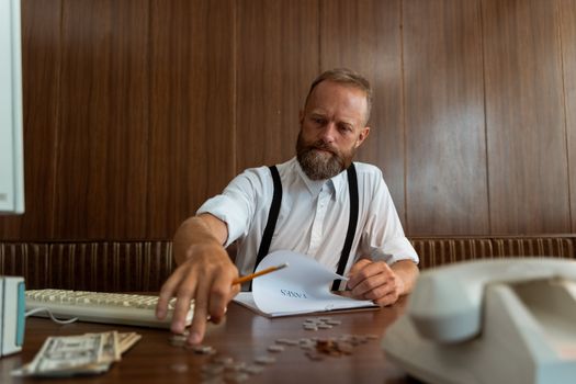 Bearded man in vintage office calculating finances with retro telephone and typewriter.