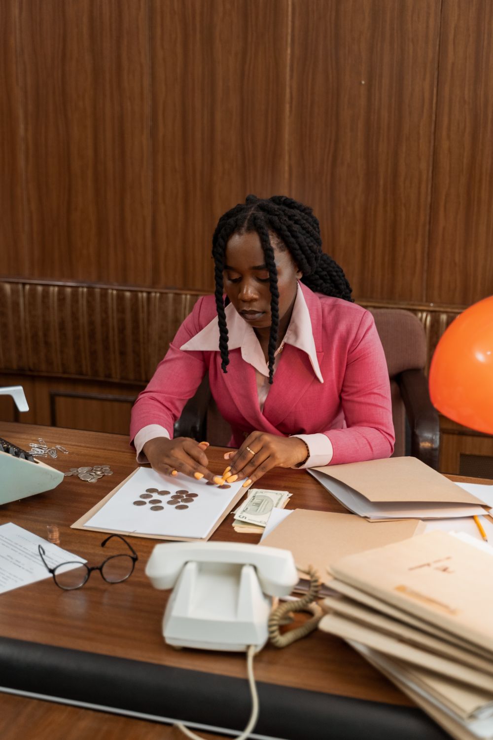 Woman in a pink blazer counting money and coins at her desk