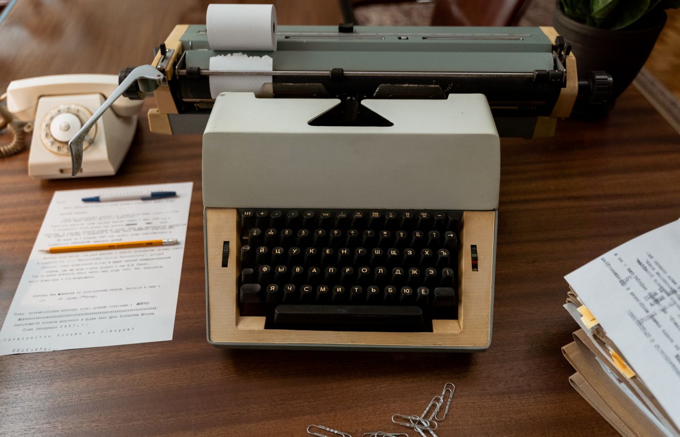 A classic workspace featuring a 70s typewriter, rotary phone, and documents on a wooden desk.