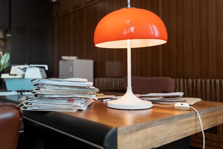 A Lamp Beside A Stack Of Documents On A Wooden Desk